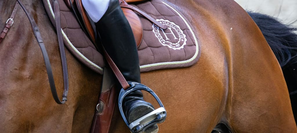 Detail of a rider's leg in tall boot and stirrup against the saddle pad